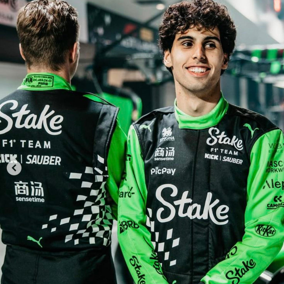 Nico Hulkenberg 2025 Racing Suit Replica – Las Vegas GP: gabriel And Nico wearing green and black racing suits with 'Stake' branding in a garage setting.