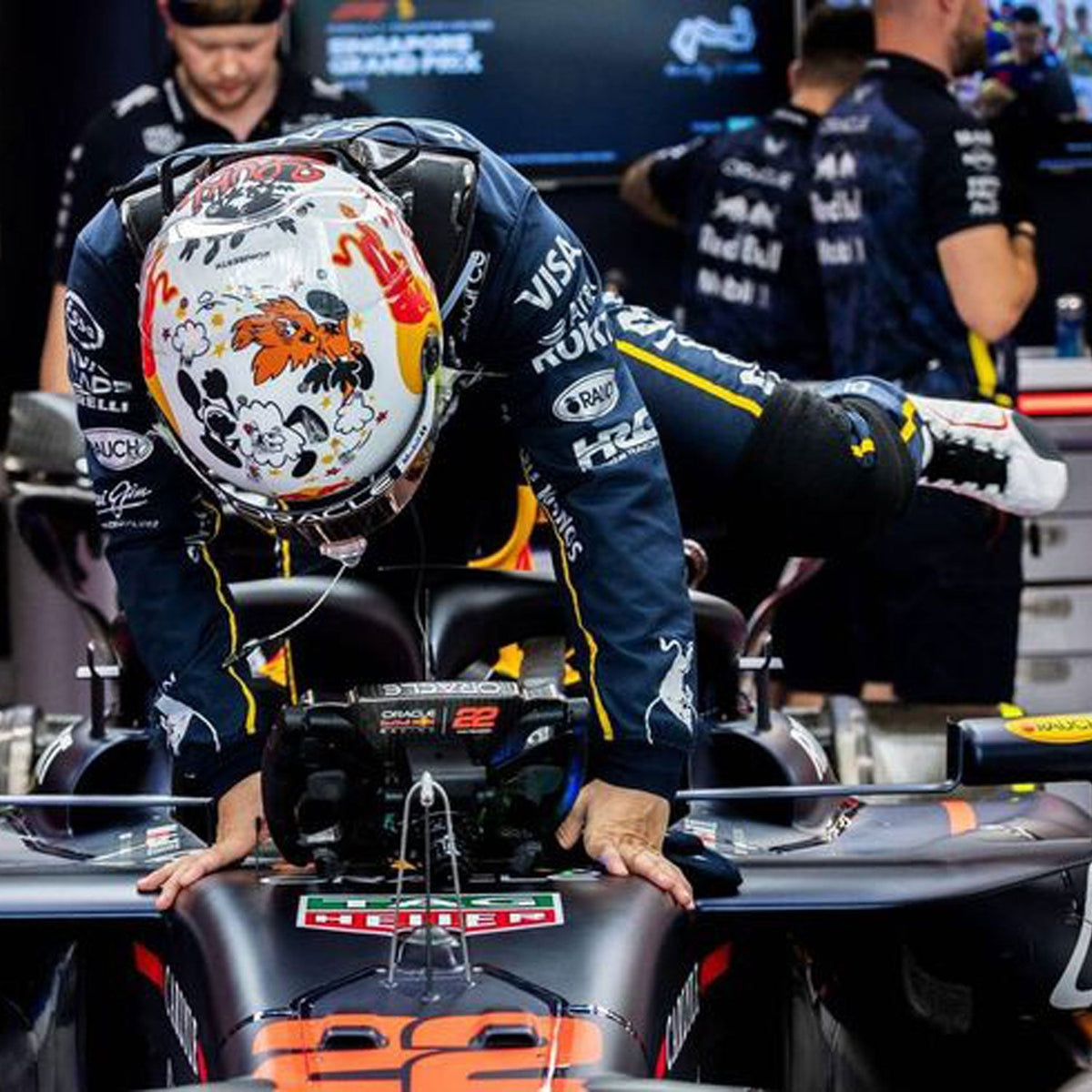 2025 Racing Suit Replica – Yuki Tsunoda Las Vegas GP: yuki Tsunoda 2025 F1 Race Costume Red Bull Las Vegas GP and helmet leaning on a Formula 1 car with logos.