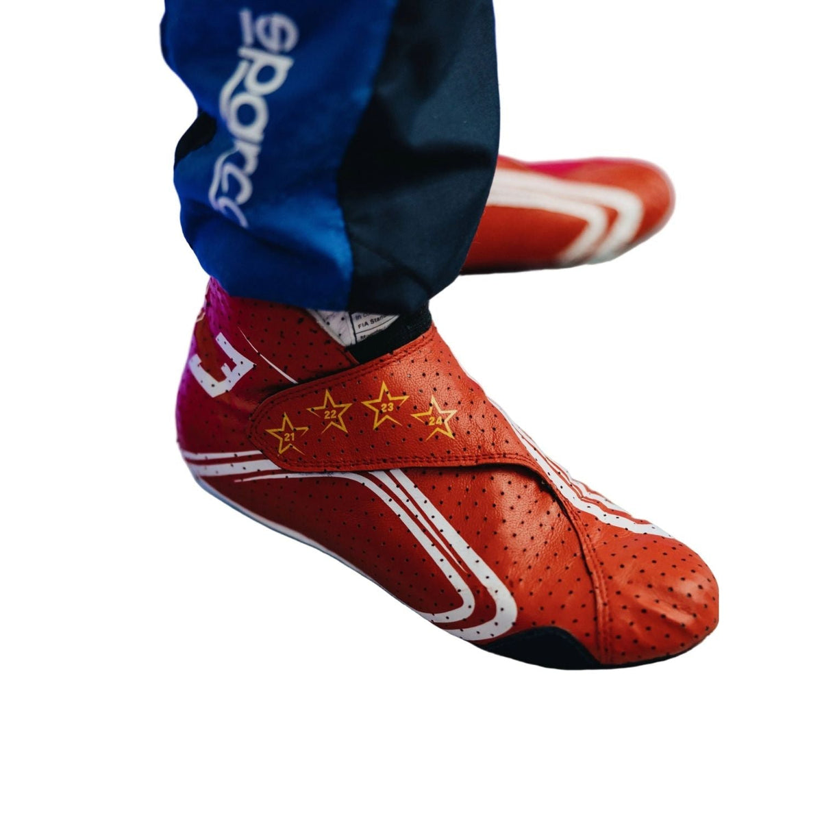 2026 Racing Shoes Replica – Max Verstappen Monaco GP: a close-up of a gymnast's foot wearing a red Sparco grip shoe with white stripes and gold stars, paired with blue and navy pants.