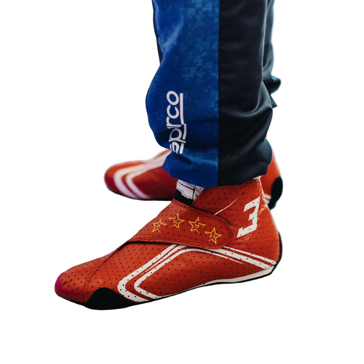 2026 Racing Shoes Replica – Max Verstappen Monaco GP: red Sparco racing shoes with white stripes and gold stars, worn with blue and black Sparco pants.