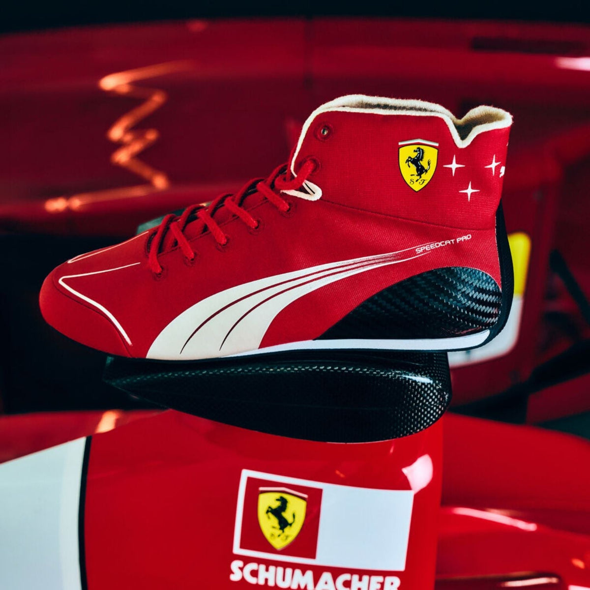 2026 Racing Shoes Replica – Italian GP: a red Puma Scuderia Ferrari high-top sneaker with white Puma stripes and a yellow Ferrari shield logo, displayed on top of a red and white Ferrari box in a dark red studio setting.