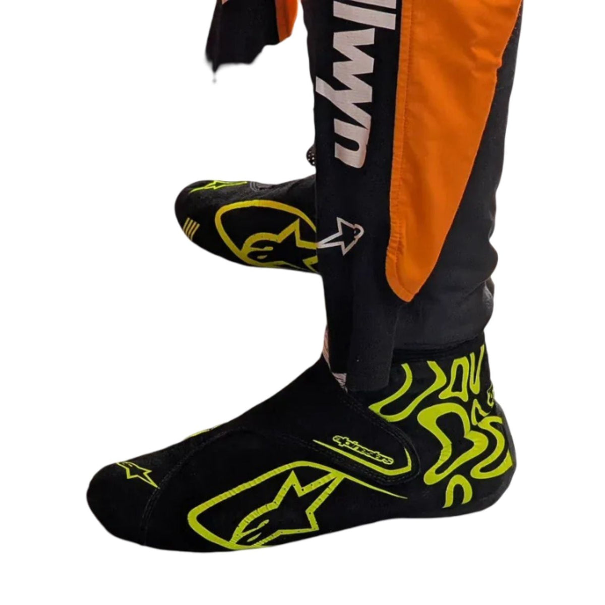 Lando Norris Racing Shoes Replica 2026: black Alpinestars foot warmers with neon yellow graphics and white Alpinestars branding, shown on a person's feet with orange and black racing pants visible against a white background.