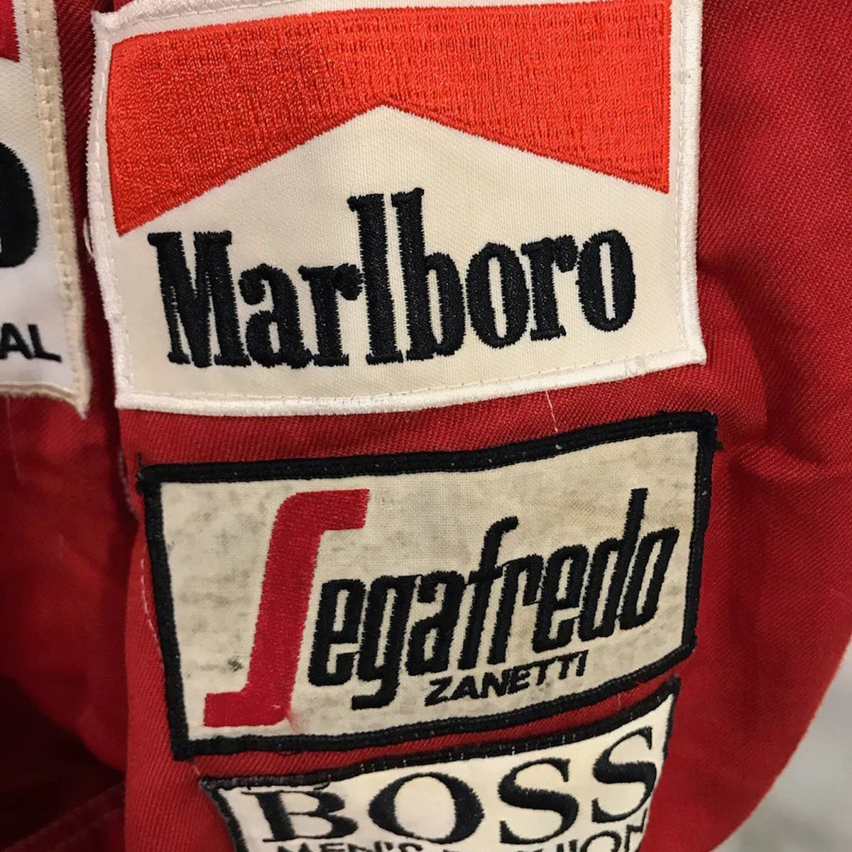 Niki Lauda Racing Suit Replica 1984: close-up of a red Niki Lauda 1984 F1 Race Costume Replica McLaren World Championship Winning Season with Marlboro, Segafredo Zanetti, and Boss logos.