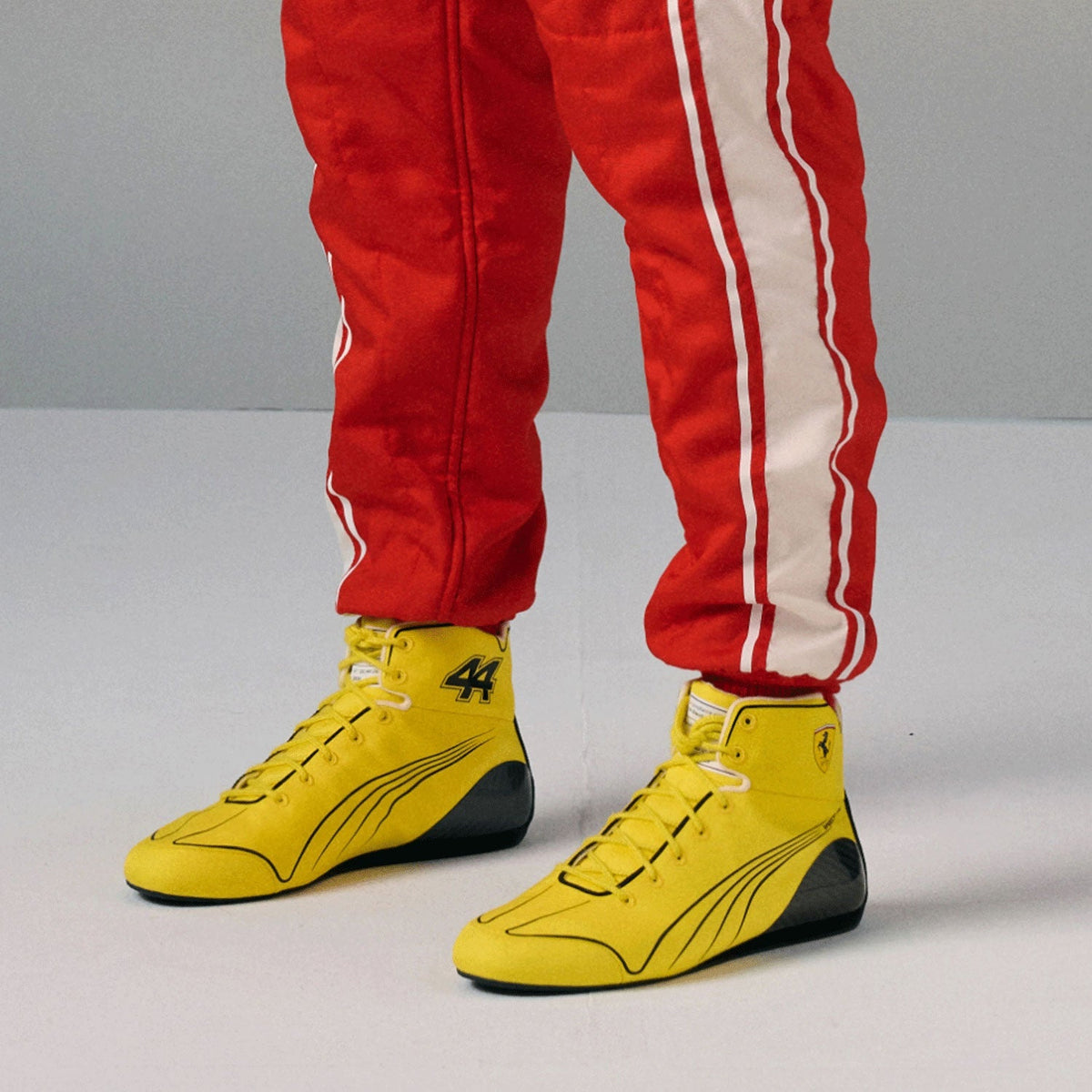 2026 Lewis Hamilton British GP Racing Shoes Replica: a pair of bright yellow high-top racing shoes with black accents, worn by a person in red and white racing pants.